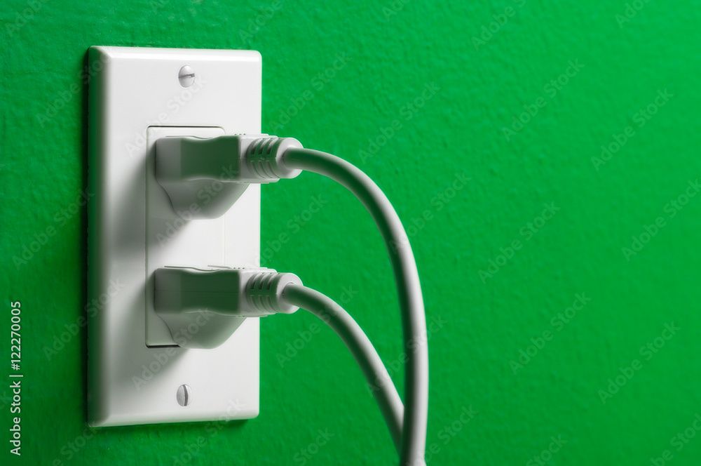 Electrical cords plugged white outlet on a green wall Electrical cords plugged white outlet on a green wall