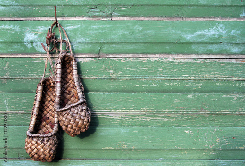 Old bast shoes (traditional russian footwear) on a green wooden photo