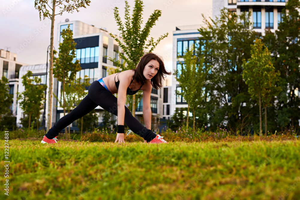 Athletic woman with strong body making fitness exercises outdoor on the green and yellow grass near modern house. Sport health life concept. Yoga female watch into camera.