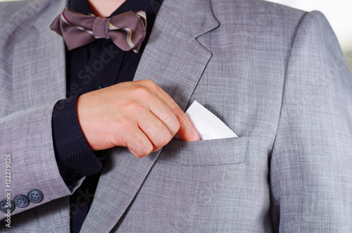 Closeup man's chest area wearing formal suit and tie, placing tissue in jacket pocket, men getting dressed concept