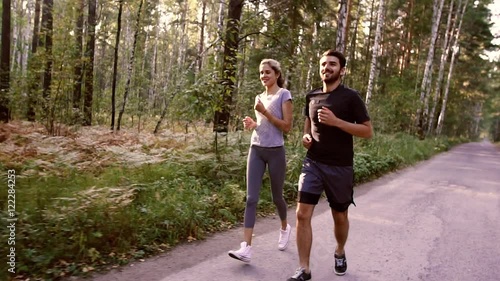 Two young people jogging together in the park full of green trees