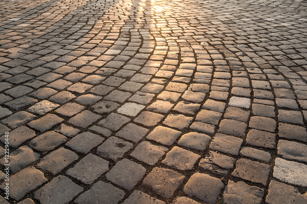 Abstract background of old cobblestone pavement close-up in sun light and shadows