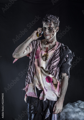 Male zombie using cell phone calling someone  standing on black smoky background  half body shot