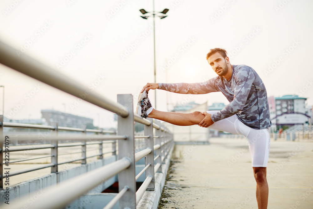 Male runner doing stretching exercise, preparing for sunset workout Male runner doing stretching exercise, preparing for sunset workout