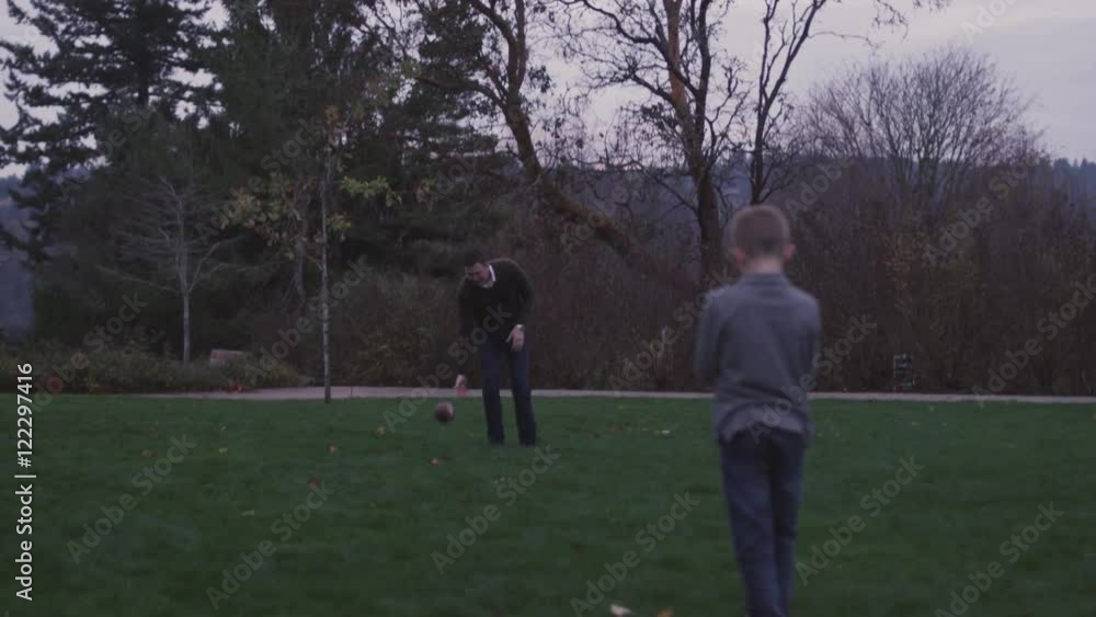 Father and son passing a football in a park at night, slow motion Father and son passing a football in a park at night, slow motion
