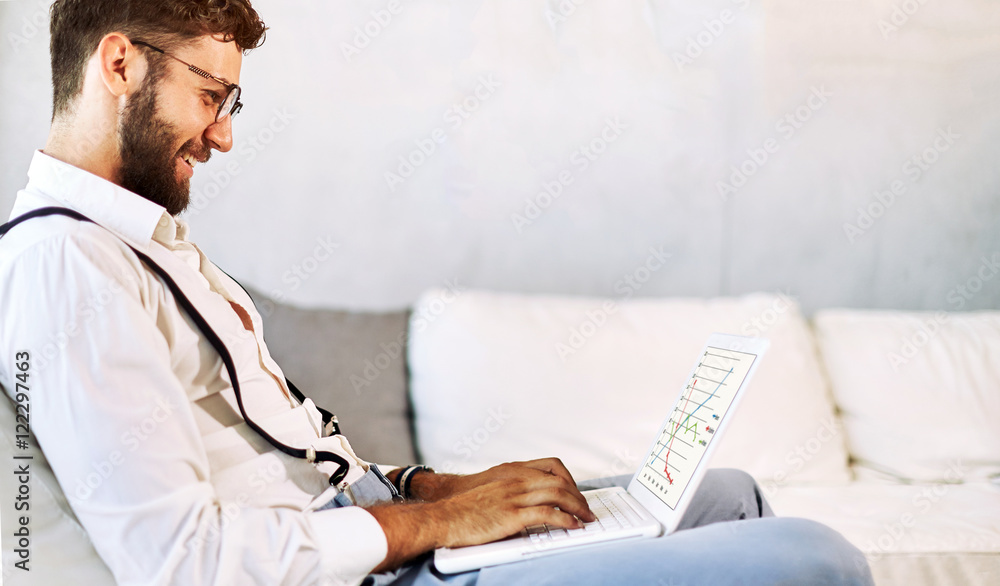 Happy young man, wearing glasses and smiling, as he works on his laptop to get all his business done early in the morning Happy young man, wearing glasses and smiling, as he works on his laptop to get all his business done early in the morning