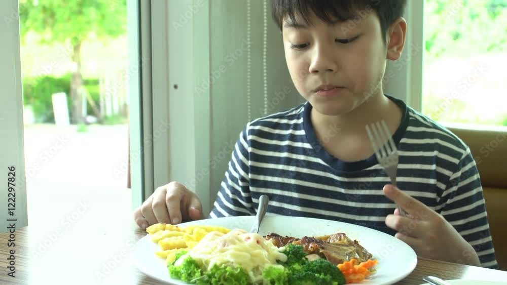 little Asian boy eating steak with vegetable Salad at restaurant with smile face little Asian boy eating steak with vegetable Salad at restaurant with smile face