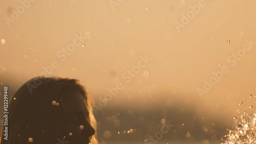 Portrait of beautiful girl splashing in the river against bright sunset