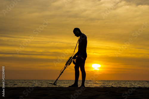 Treasure hunter with Metal detector on sunset the beach