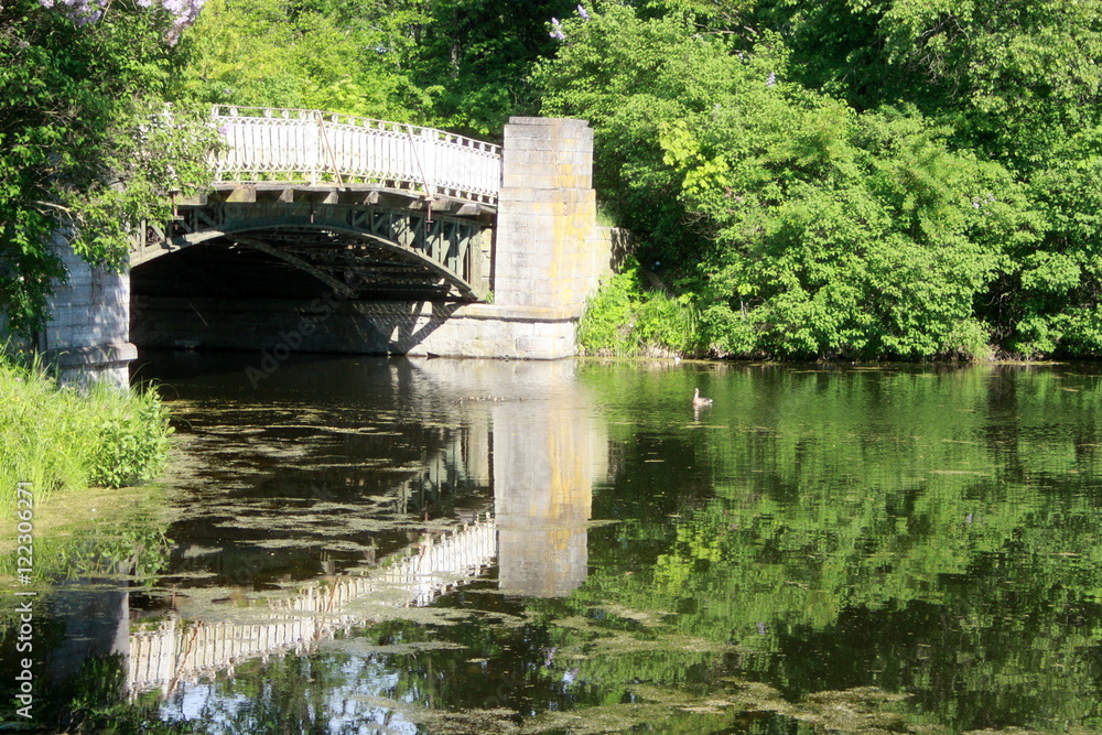 White stone bridge and green trees reflected in the pond
