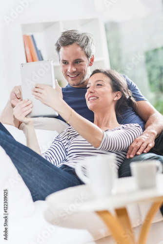 Cheerful couple sitting on a white couch at home using a tablet