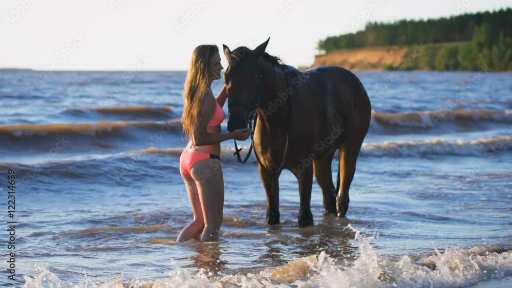 A beautiful blonde young sexy woman standing next to a horse at a lake A beautiful blonde young sexy woman standing next to a horse at a lake