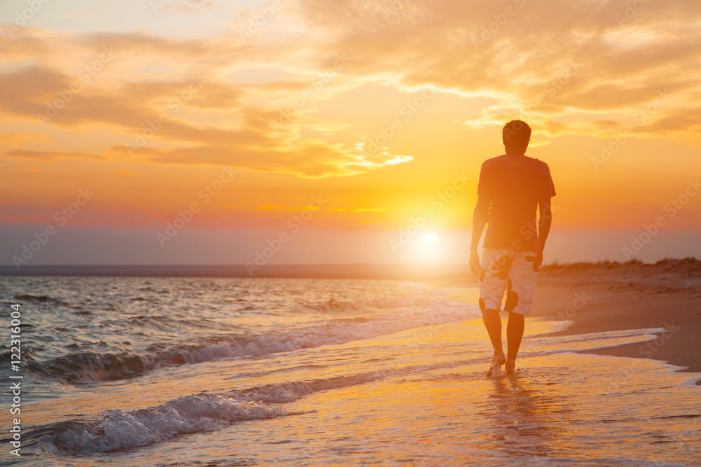 silhouette of a young man who walks on the beach, against the backdrop of a beautiful sunset