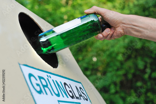 Mensch entsorgt eine Glasflasche in einem Altglas-Container photo