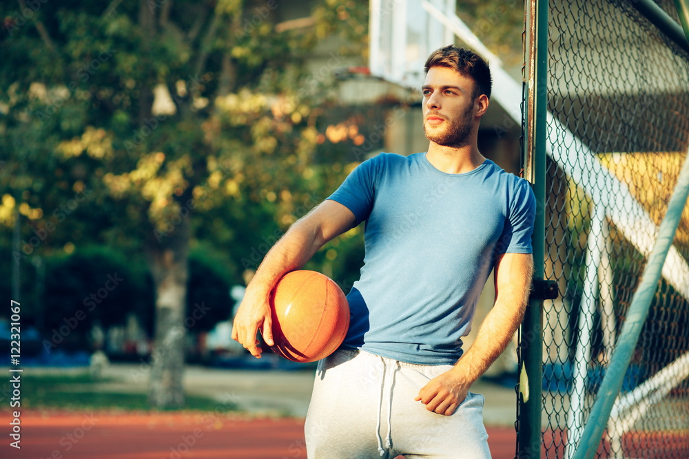Obraz premium Handsome young man posing with a ball on the basketball court
