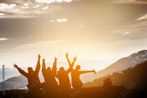 Group of friends sits on the top of mountain and having fun on mountains backdrop