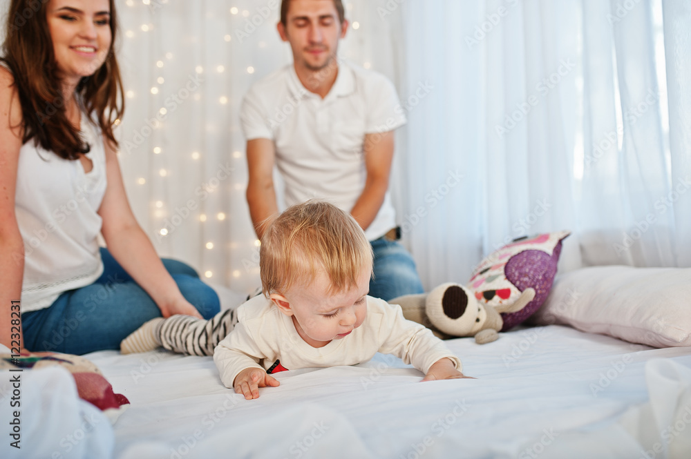 Mother and father with baby boy sitting on white bed with garlan Mother and father with baby boy sitting on white bed with garlan