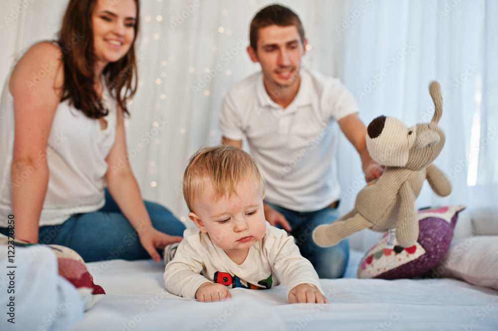 Mother and father with baby boy sitting on white bed with garlan Mother and father with baby boy sitting on white bed with garlan