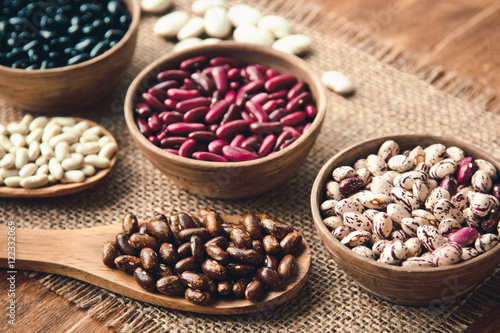 Beautiful multi-colored beans in bowls and wooden spoons on a background of burlap