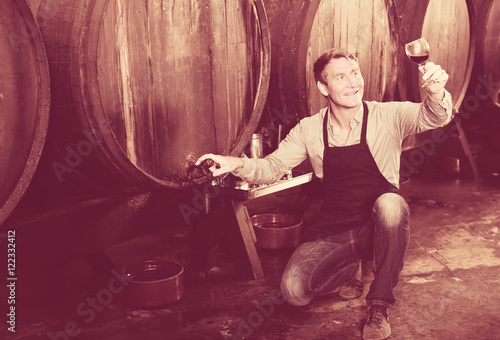 winemaker holding glass of wine in cellar.