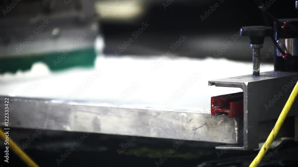 A pneumatic silk screening printing press operates. A pneumatic silk screening printing press operates.