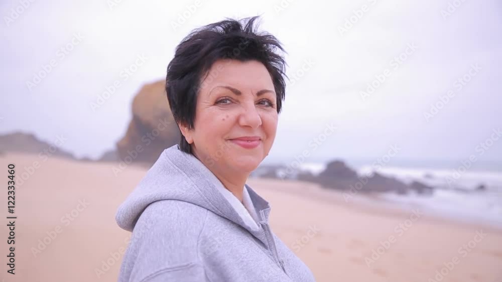 Attractive active mature woman standing on an ocean beach and smiling at camera.