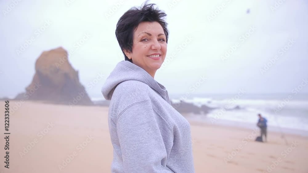 Attractive active mature woman standing on an ocean beach and smiling at camera. Attractive active mature woman standing on an ocean beach and smiling at camera.