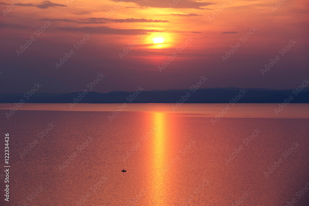 sunset on the lake and a lonely fisherman boat with golden reflection - for book cover or web design sunset on the lake and a lonely fisherman boat with golden reflection - for book cover or web design