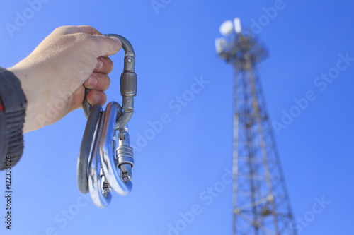 carabiners for work at height on telecommunication towers. tower climber holds in hand a bunch of carabiners for mountaineering on the background of blue sky and telecommunication tower