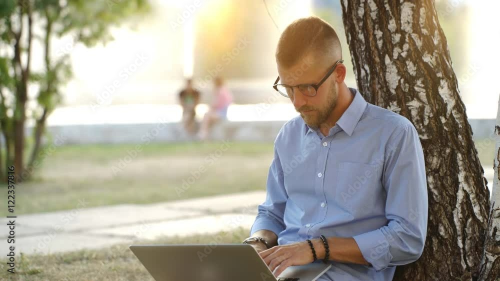 Man is Sitting at the park, Sitting on the Ground,Working with Laptop Freelance Man is Sitting at the park, Sitting on the Ground,Working with Laptop Freelance