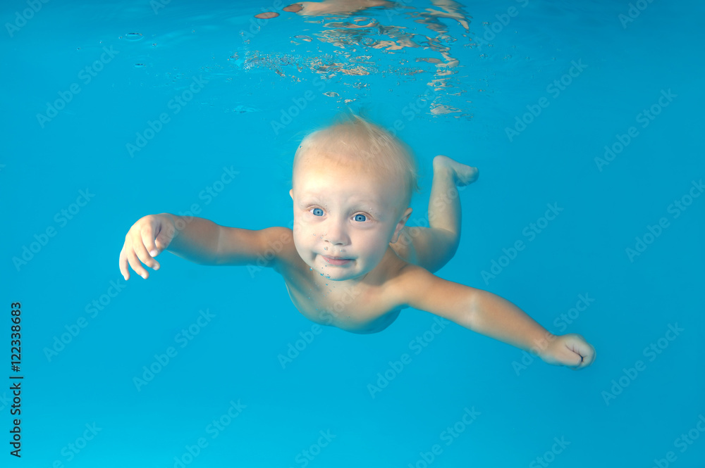 Beautiful blue-eyed blond baby boy swims underwater on a blue water background. Healthy family lifestyle and children water sports activity. Child development, disease prevention