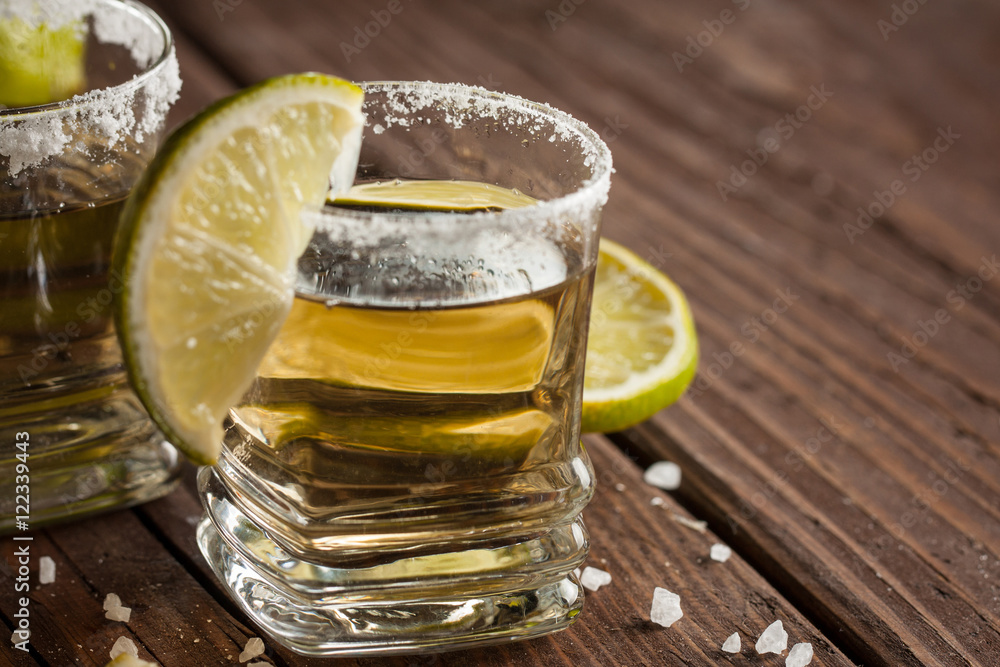 Macro focus photo of shots of golden Mexican tequila with lime and salt on wooden background. Alcoholic drink concept. Macro focus photo of shots of golden Mexican tequila with lime and salt on wooden background. Alcoholic drink concept.