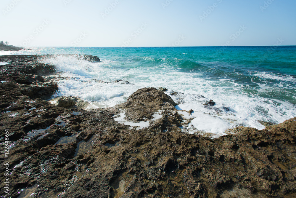High waves of the Caribbean Sea are splashing hardly against cliffs and rocks on a coastline at hot summer sunny day