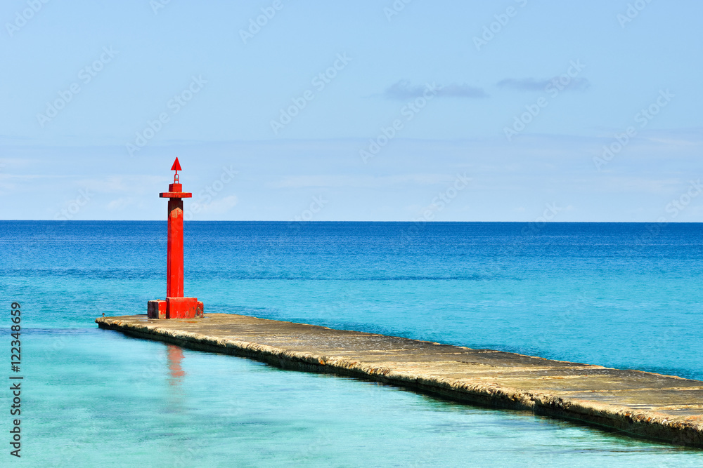 High red color sea lighthouse is on the deserted pier. Beautiful landscape of the coastline of the Caribbean Sea at summer sunny day