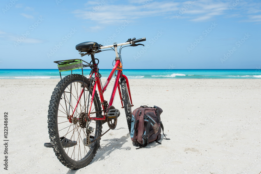 Bicycle is perked on the coast of Caribbean Sea with snow-white sand. Backpack and slates lie nearby.