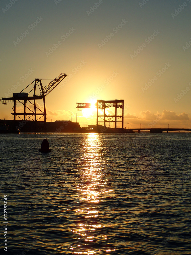 Obraz premium Sunset through Hoisting cranes at container cargo terminals