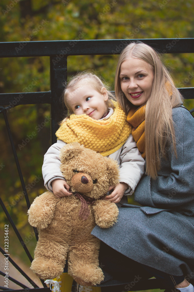The mother, her daughter and toy Teddy bear posing and walking in autumn park, close up The mother, her daughter and toy Teddy bear posing and walking in autumn park, close up