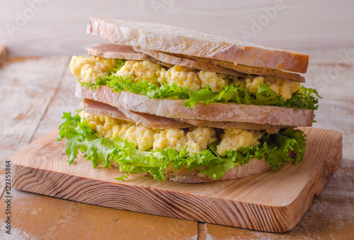 Sandwich with scramble eggs, leaves salad and ham on wooden baskgraund. Selective focus photo