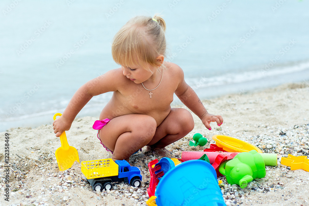 Adorable toddler girl playing with beach toys on white sand beach Adorable toddler girl playing with beach toys on white sand beach
