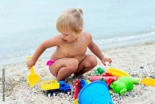 Adorable toddler girl playing with beach toys on white sand beach