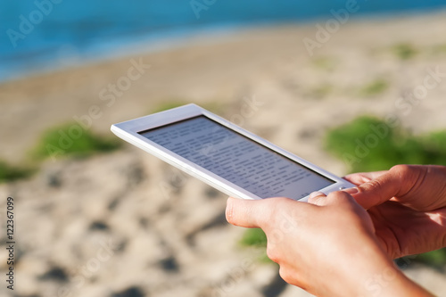 wooman sitting on sandy beach and holding bookreader photo