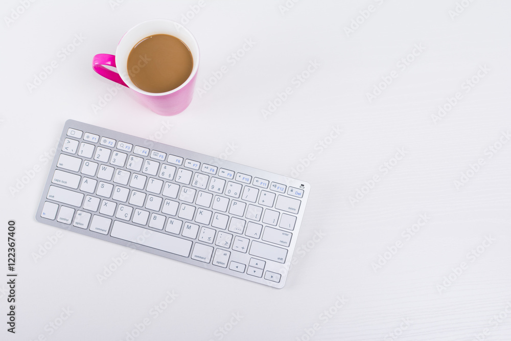 White and silver wireless keyboard and pink cup of coffee on white wooden table White and silver wireless keyboard and pink cup of coffee on white wooden table