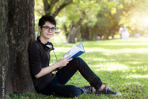 Asian young handsome man student reading book in nature.