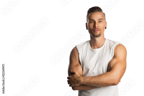 Well trained and attractive man wearing a white tank top standing against a white background with his arms crossed.