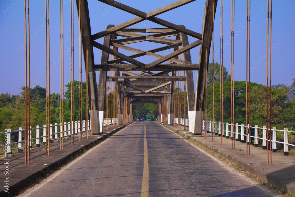 Road and a small suspension bridge in countryside of Thailand.