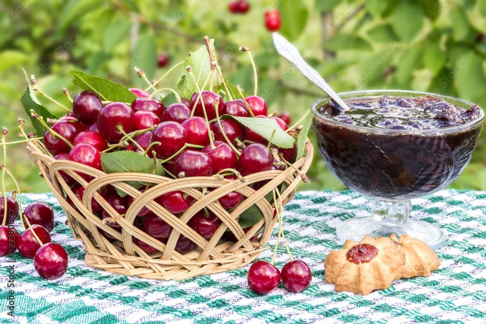 Basket of cherries and cherry jam with biscuit on background of cherry tree Basket of cherries and cherry jam with biscuit on background of cherry tree
