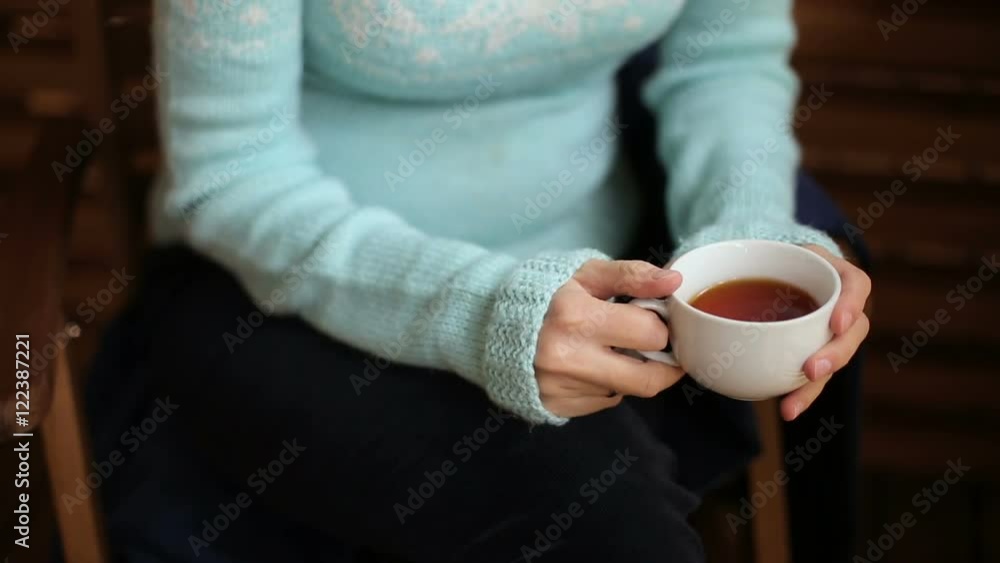 girl in a blue sweater sitting on a wooden chair and drinking tea girl in a blue sweater sitting on a wooden chair and drinking tea
