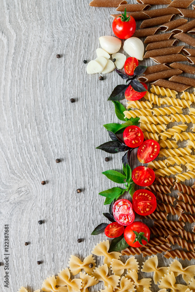 Mixed of two colored pasta near tomatoes, garlic and basil on grey wooden background. Raw frame. Copy space. Mixed of two colored pasta near tomatoes, garlic and basil on grey wooden background. Raw frame. Copy space.