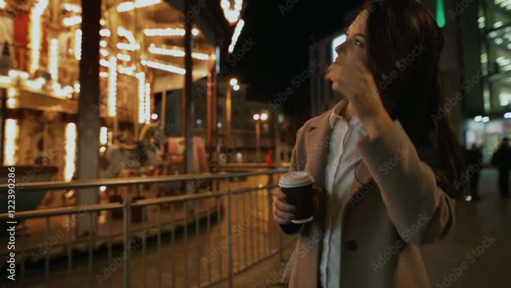 Woman walking in night city and contemplate illuminated carousel Woman walking in night city and contemplate illuminated carousel