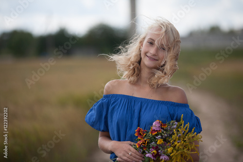 The girl in the blue dress in a field with bouquet of flowers